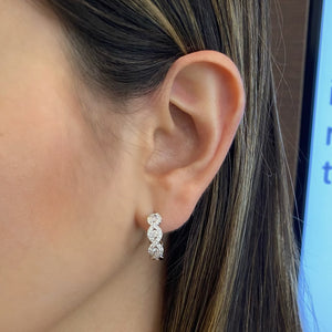 Female model wearing Diamond Twist hoop earrings - 18K gold weighing 5.83 grams  - 6 round diamonds totaling 0.30 carats  - 54 round diamonds totaling 0.50 carats