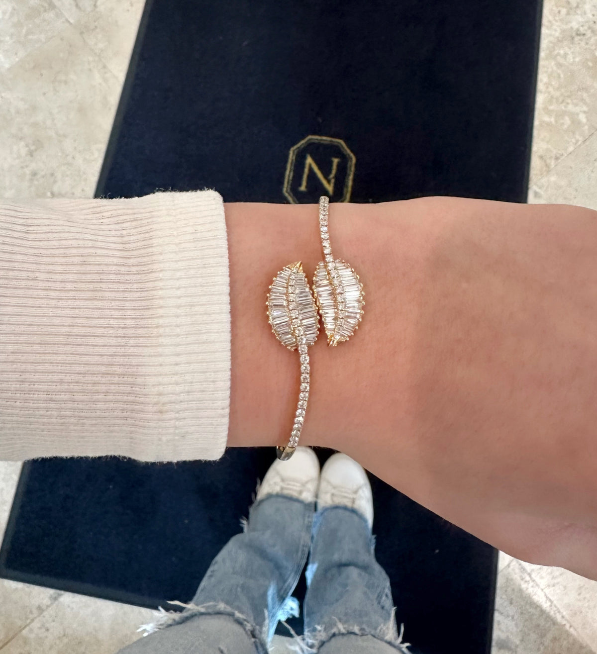 Female model wearing Diamond Bypass Leaf Bangle - 14kt yellow gold 12.60 grams - 56 straight baguettes weighing 1.50 ct - 46 round brilliant cut diamonds weighing 0.83 ct