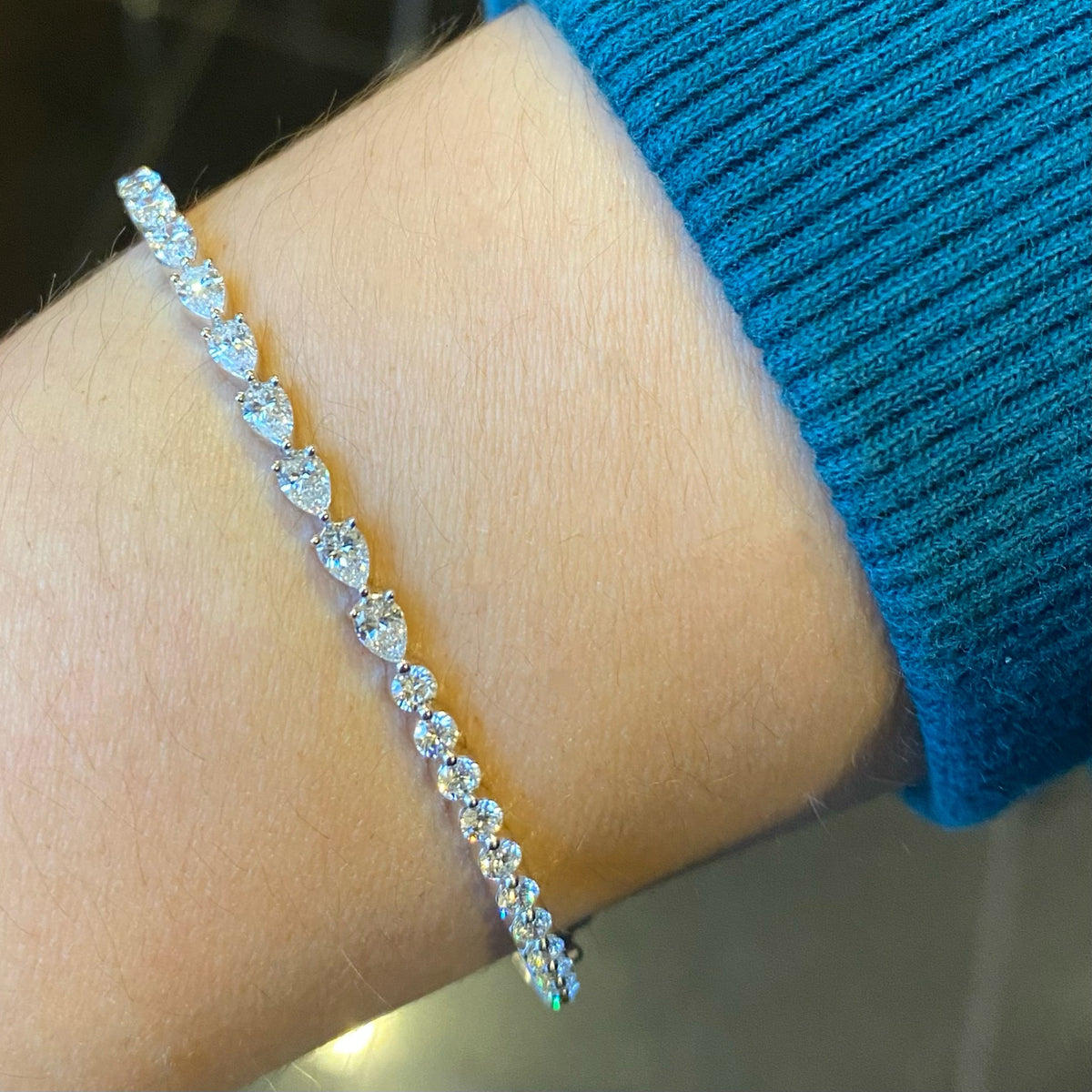 Female Model Wearing Round & Pear-Shaped Diamond Bangle Bracelet - 18K gold weighing 11.06 grams - 12 round diamonds weighing 0.68 carats - 9 pear-shaped diamonds weighing 0.96 carats