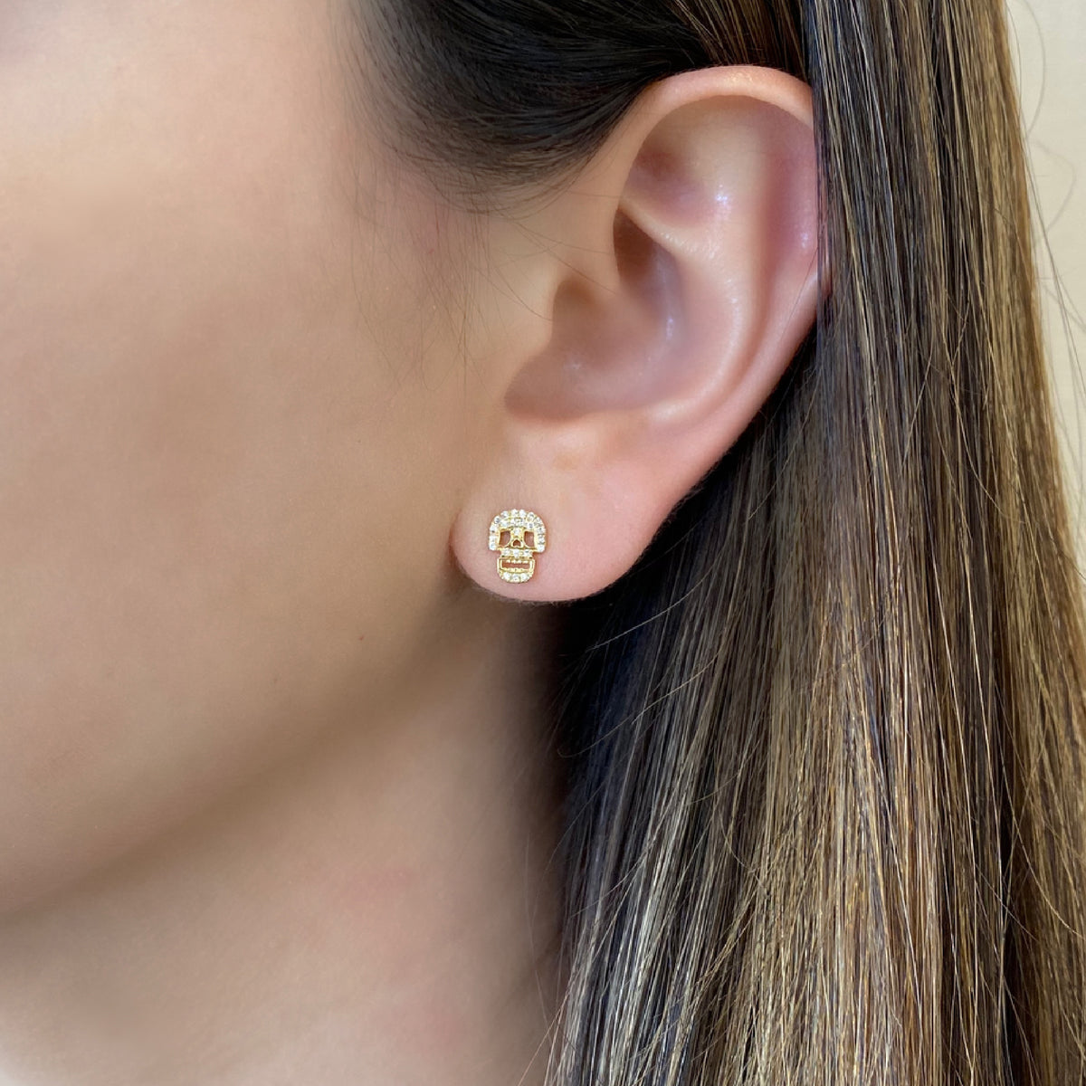 Female model wearing Diamond Skull Cutout Stud Earrings - 14K gold weighing 1.36 grams - 46 round diamonds weighing 0.12 carats