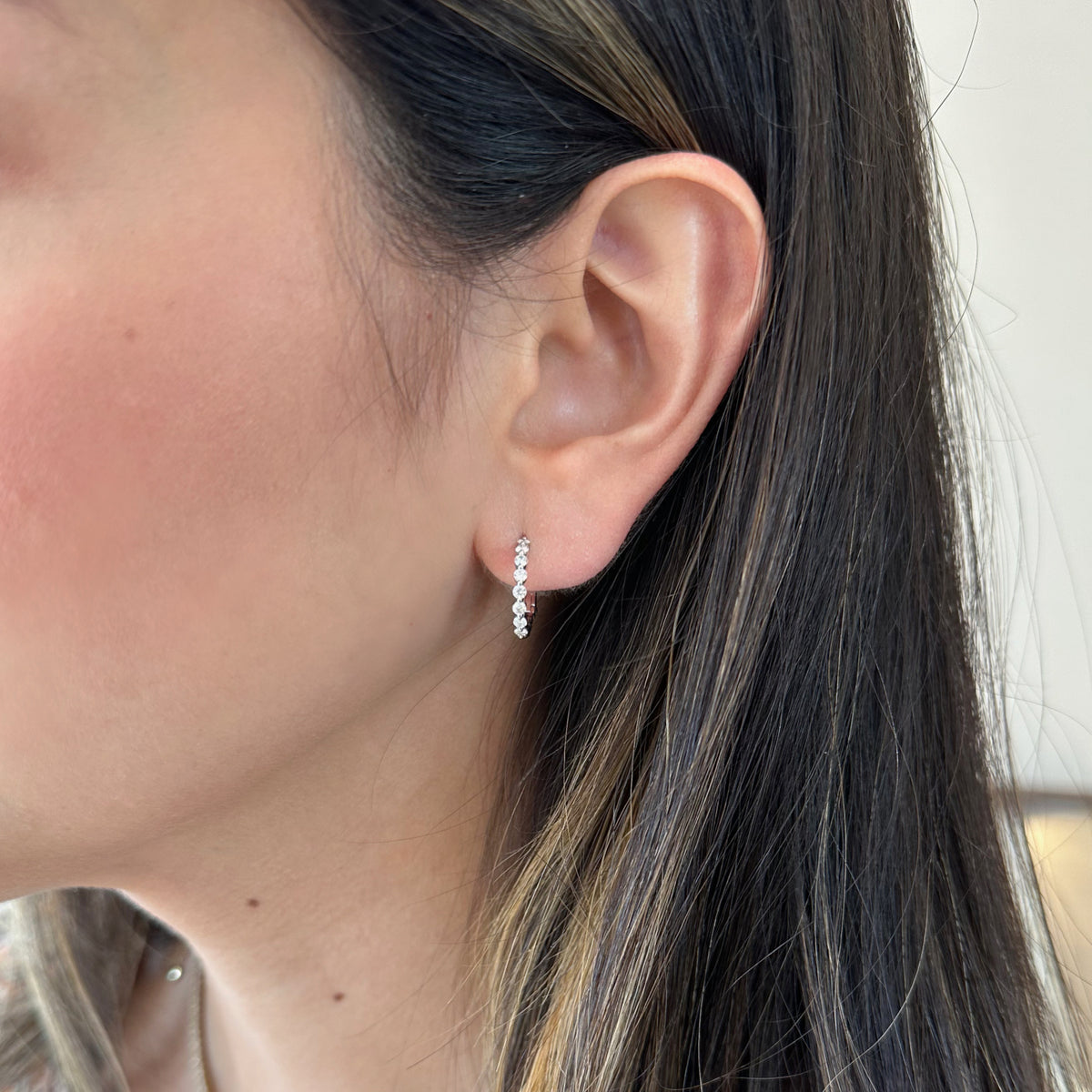 Female model wearing Shared Prong Diamond Huggie Earrings - 18K gold weighing 2.50 grams - 16 round diamonds weighing 0.46 carats