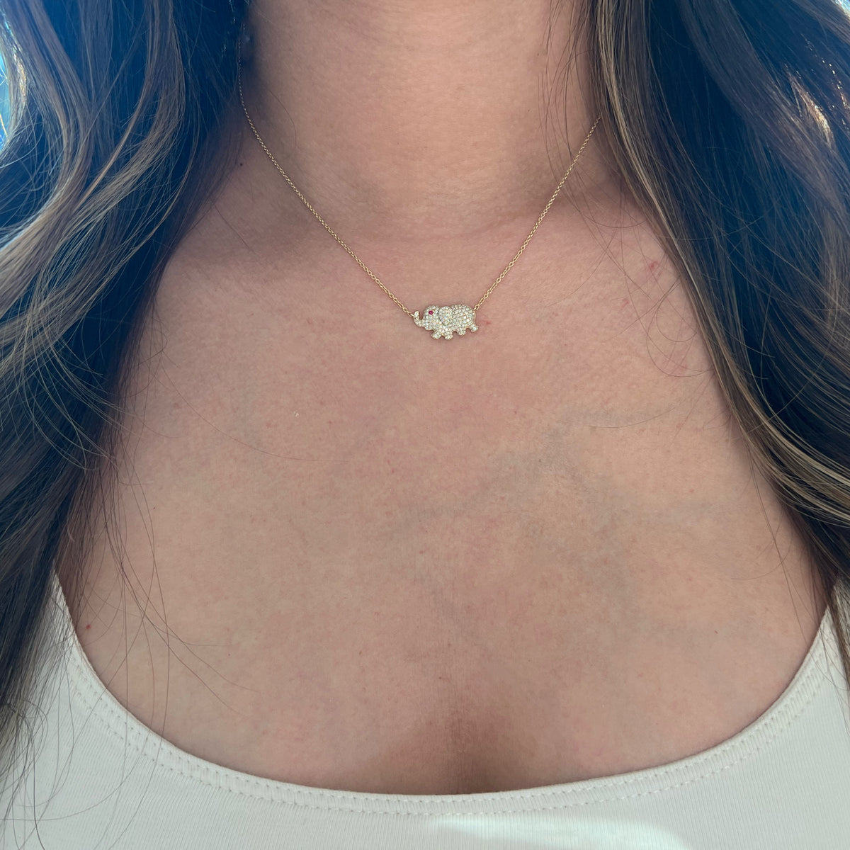 Female model wearing Pave Diamond Elephant Pendant Necklace  -14k yellow gold weighing 3.30 grams  -145 round diamonds weighing 0.48 carats  -1 ruby weighing 0.02 carats