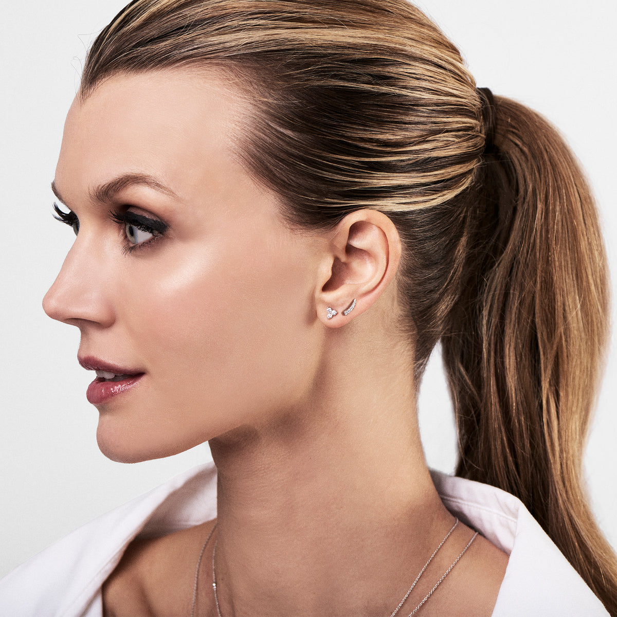 Female model wearing Diamond Three Stone Stud Earrings -14k gold weighing .80 grams -6 round diamonds weighing .32 grams 