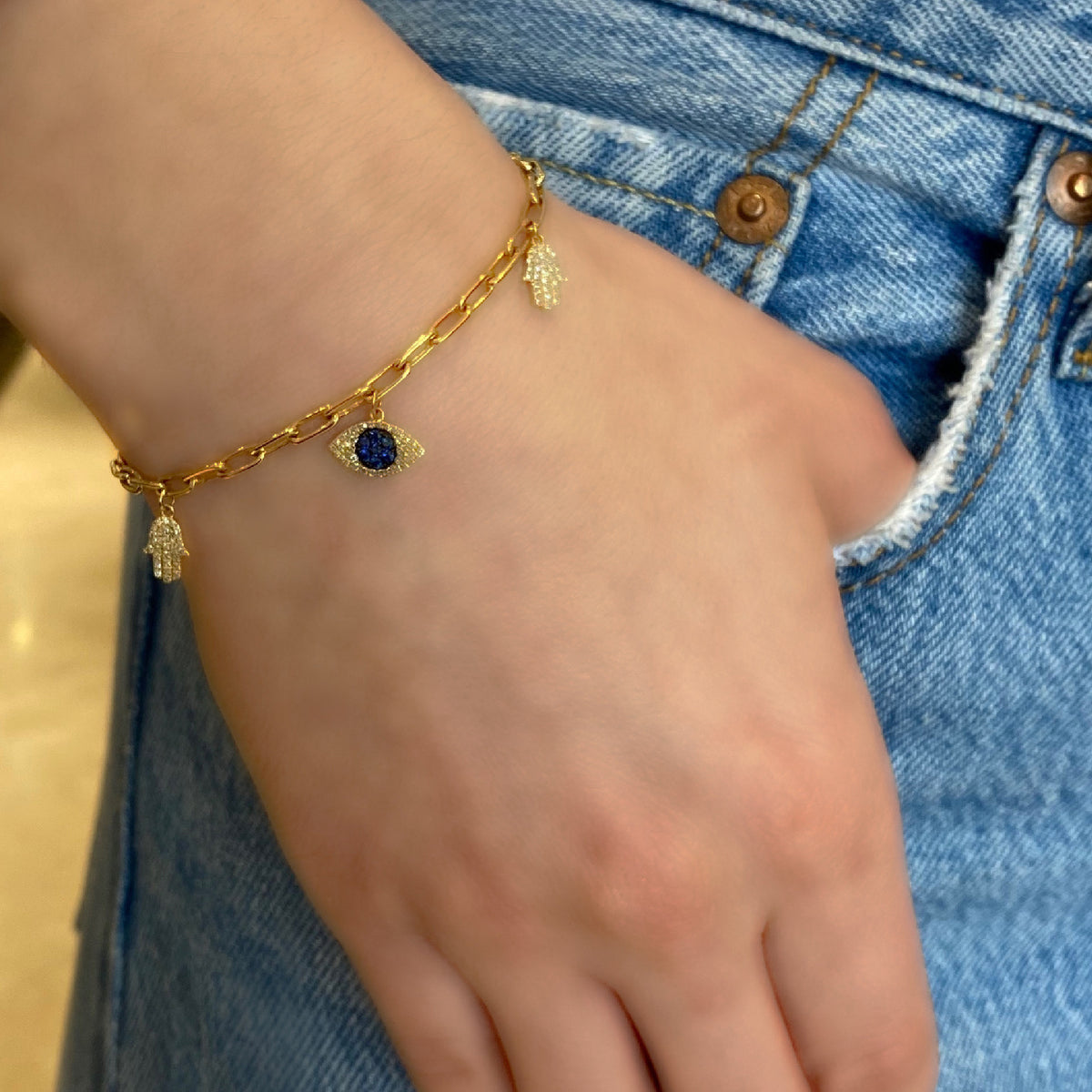 Female model wearing Diamond & Sapphire Evil-Eye & Hamsa Charm Bracelet -14K gold weighing 5.86 grams -138 round diamonds totaling 0.32 carats -9 sapphires totaling 0.20 carats