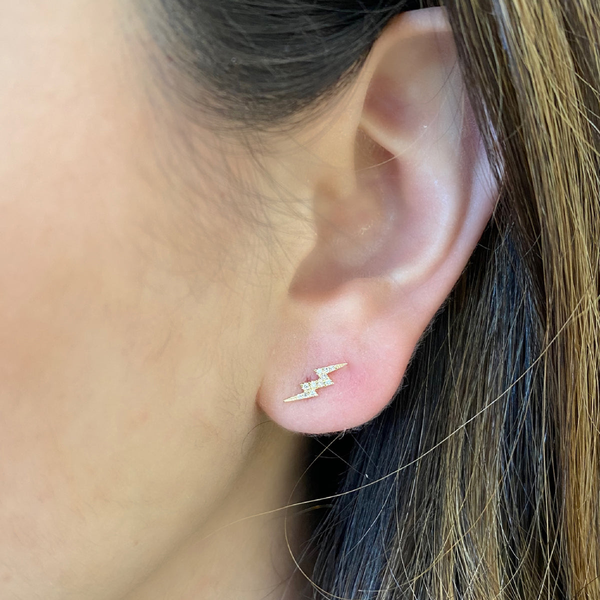 Female model wearing Diamond Star & Lightning Bolt Stud Earrings - 14K yellow gold weighing 0.90 grams - 23 round diamonds totaling 0.06 carats.