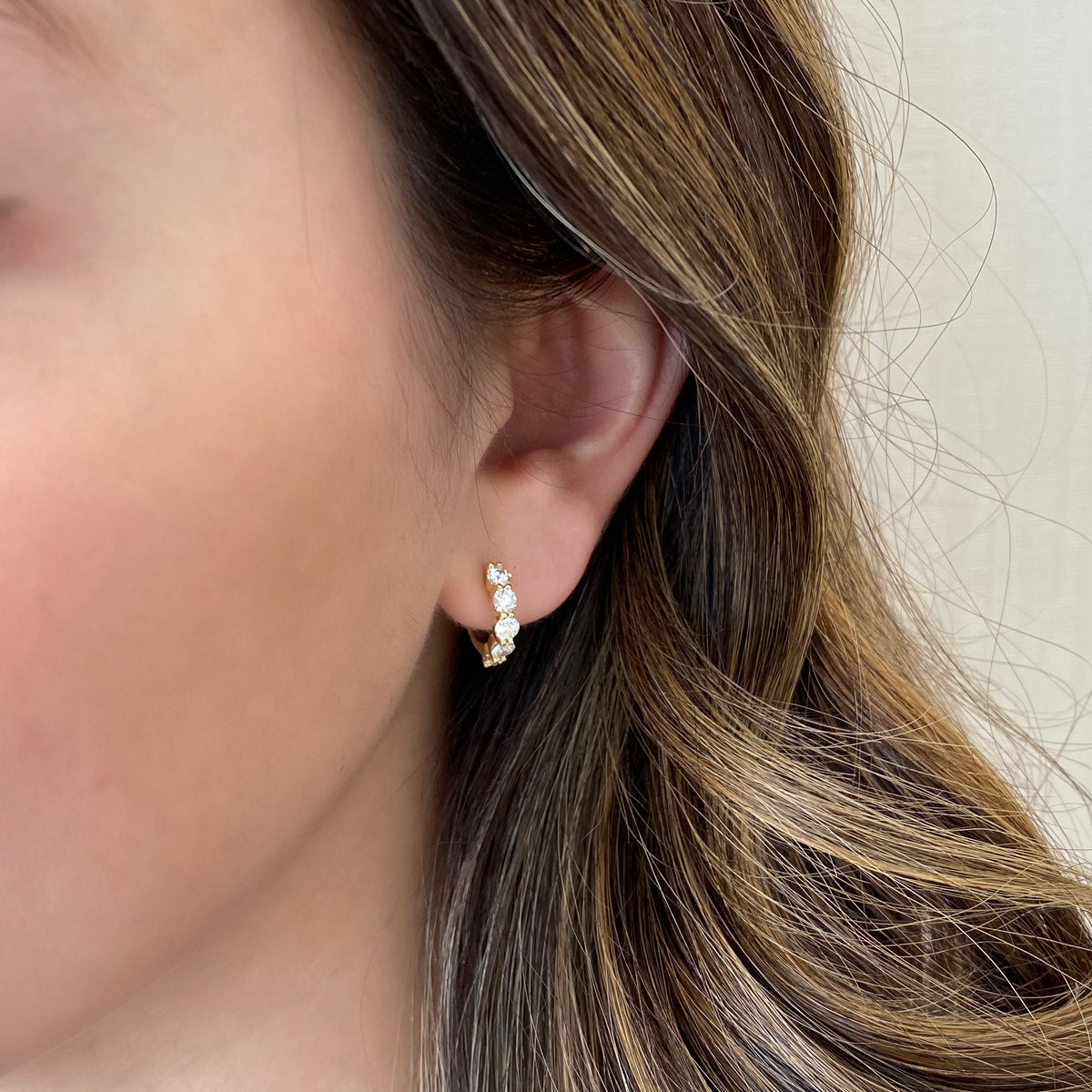 Female model wearing Round diamond huggie earrings -14K yellow gold weighing 3.08 grams -10 round diamonds totaling 1.10 carats