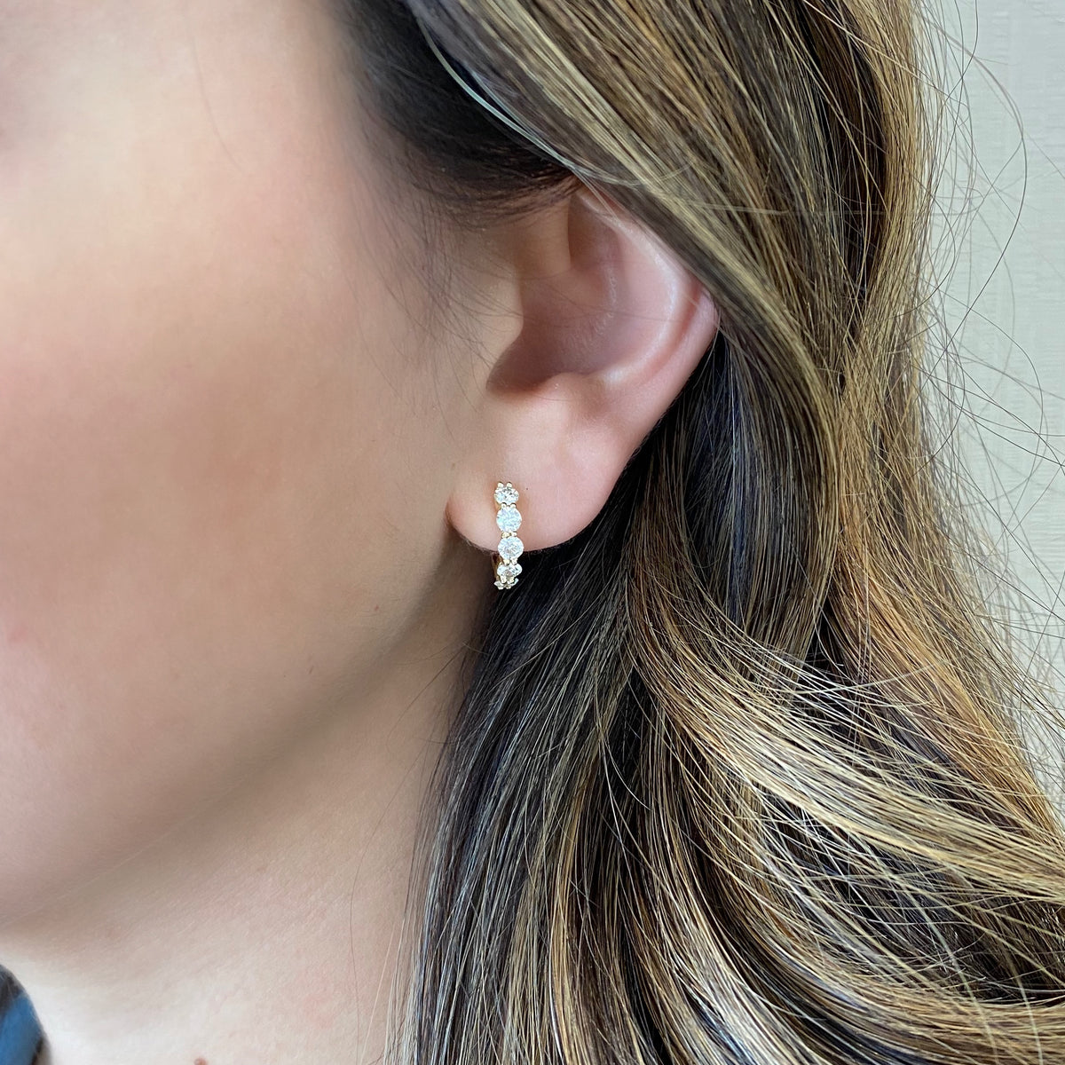 Female model wearing Round diamond huggie earrings -14K yellow gold weighing 3.08 grams -10 round diamonds totaling 1.10 carats