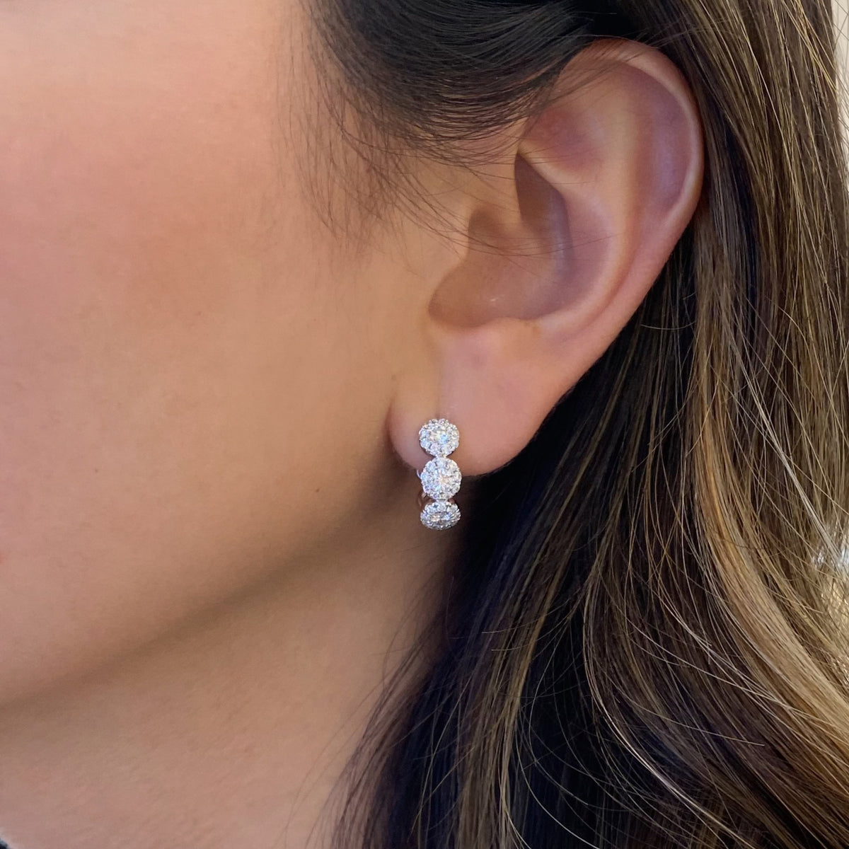 Female Model Wearing Halo Diamond Huggie Earrings - 18K gold weighing 4.23 grams  - 6 round diamonds weighing 0.65 carats  - 54 round diamonds weighing 0.57 carats