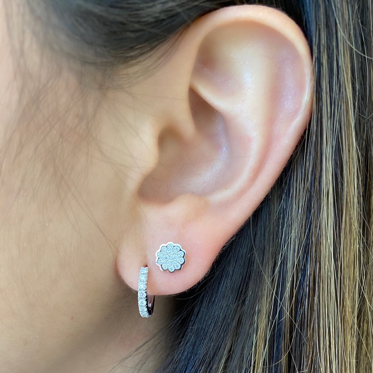 Female model wearing Diamond Floral Stud Earrings - 14K gold weighing 1.82 grams - 28 round diamonds totaling 0.18 carats