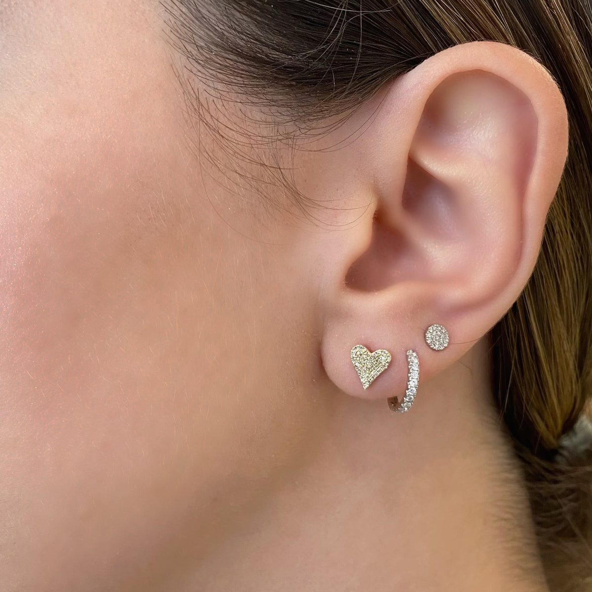 Female model wearing Pave Diamond Heart Stud Earrings - 14K yellow gold weighing 1.10 grams - 76 round diamonds totaling 0.19 carats