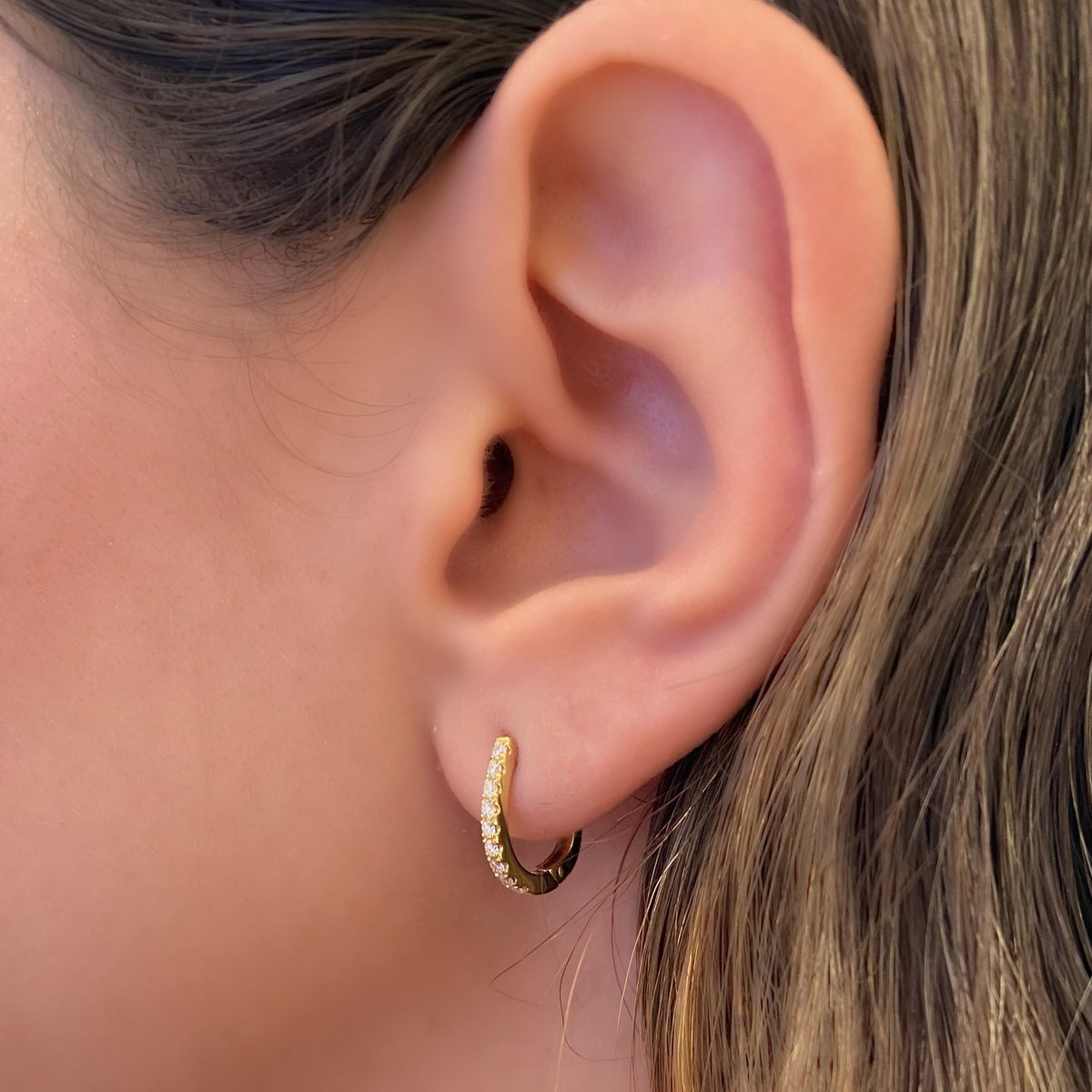 Female Model Wearing Diamond Small Horseshoe Huggie Earrings - 18K gold weighing 2.10 grams  - 18 round diamonds totaling 0.26 carats