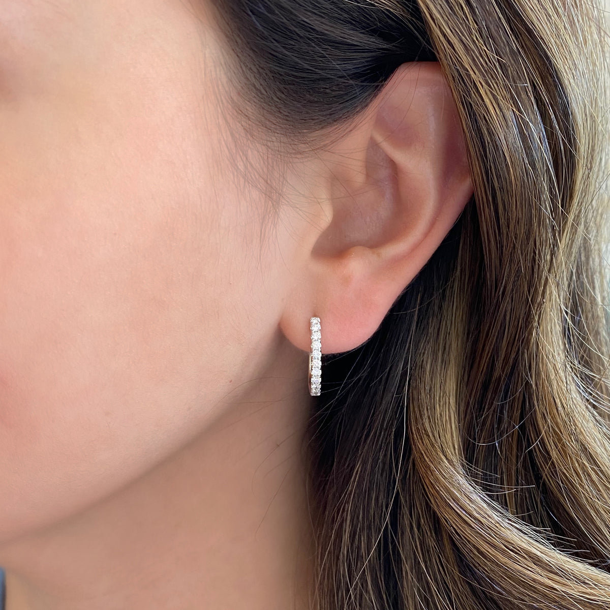 Female model wearing Diamond huggie earrings 18k gold, 3.49 grams, 22 round shared prong-set diamonds .44 carats.  Earring size 16.5 millimeters, width 2 millimeters.