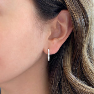Female model wearing Diamond huggie earrings 18k gold, 3.49 grams, 22 round shared prong-set diamonds .44 carats.  Earring size 16.5 millimeters, width 2 millimeters.