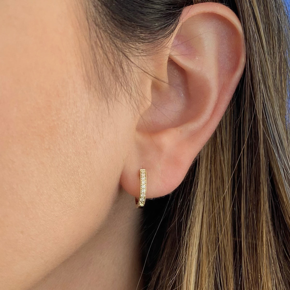 Female Model Wearing Diamond Small Huggie Earrings With Milgrain Detail - 14K gold weighing 1.99 grams  - 16 round diamonds totaling 0.14 carats
