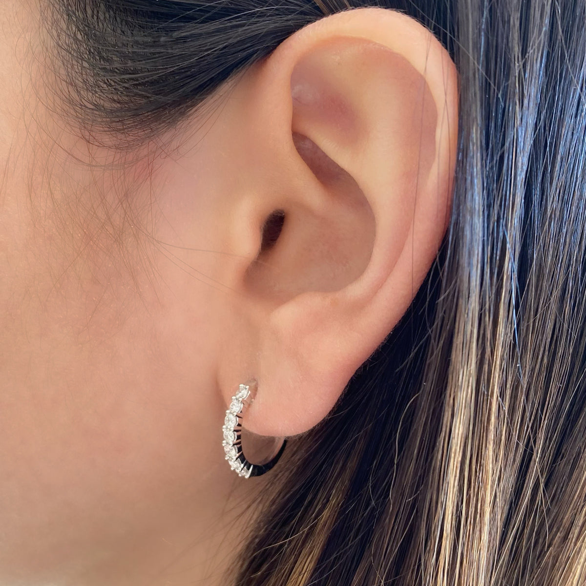 Female model wearing Prong-set diamond huggie earrings - 18K gold weighing 2.68 grams  - 14 round diamonds totaling 0.56 carats