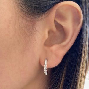 Female model wearing Prong-set diamond huggie earrings - 18K gold weighing 2.68 grams  - 14 round diamonds totaling 0.56 carats