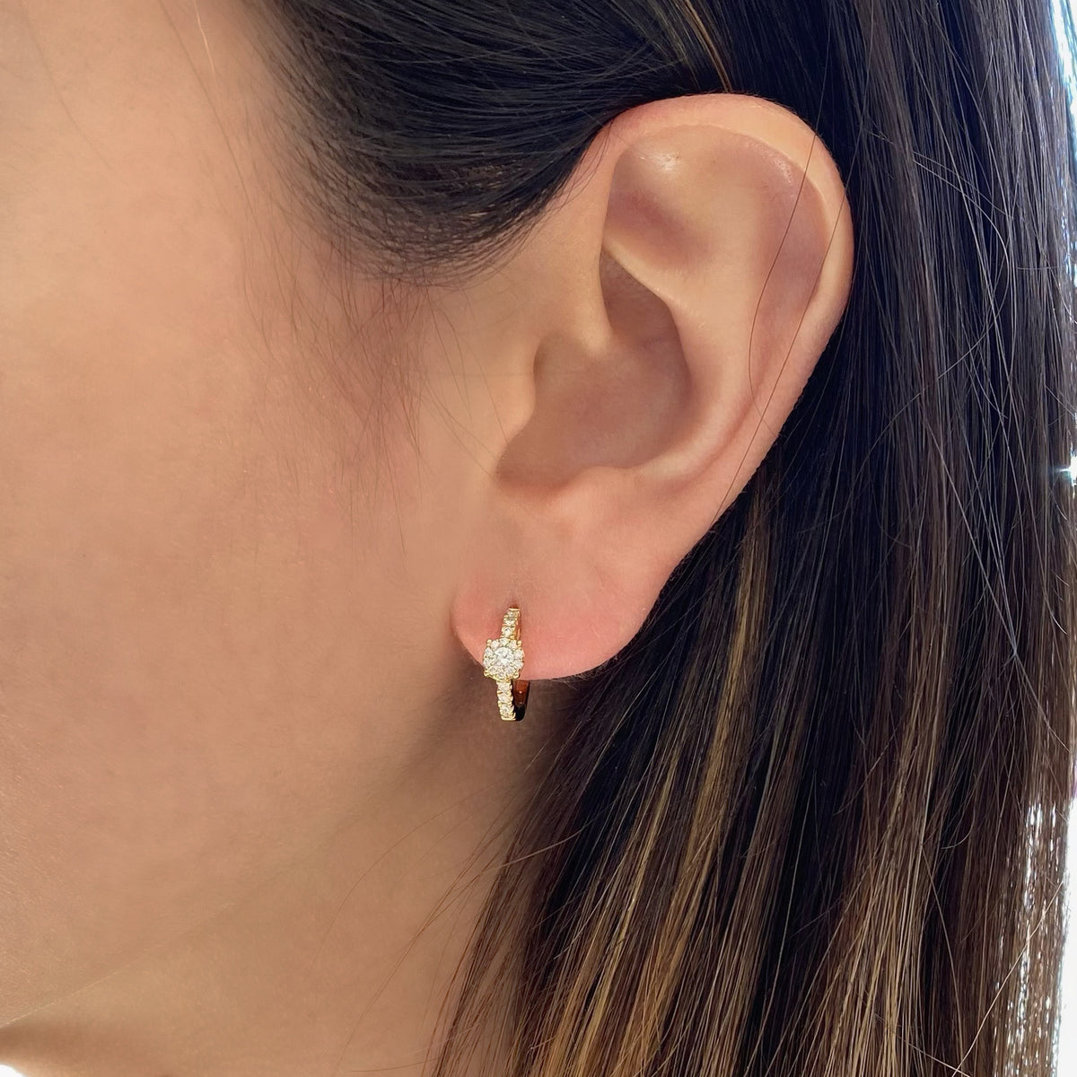 Female model wearing Diamond halo huggie earrings - 18K gold weighing 2.50 grams - 34 round diamonds totaling 0.21 carats - 2 round diamonds totaling 0.10 carats