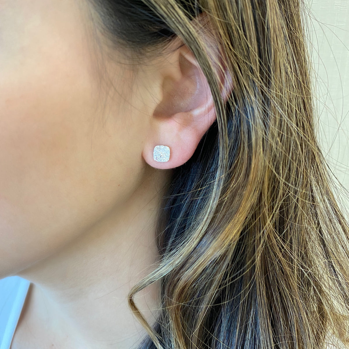 Female model wearing Diamond small cushion-shaped stud earrings - 18K gold weighing 2.15 grams  - 18 round diamonds totaling 0.71 carats