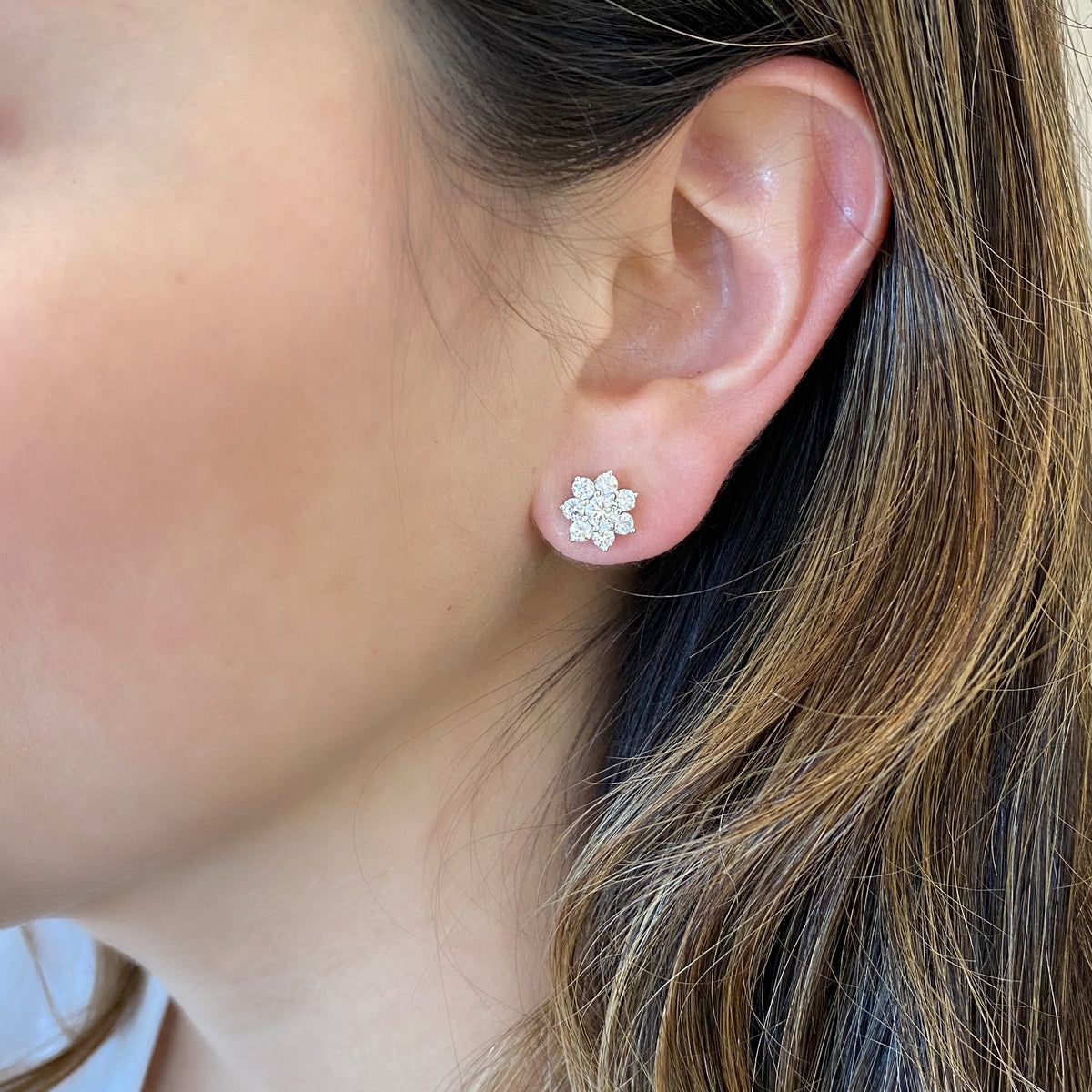female model wearing diamond flower stud earrings  crafted with 18k gold, 2.65 grams, 14 round shared prong-set diamonds 1.0 carats, 2 round shared prong-set diamonds .41 carats, post closure.