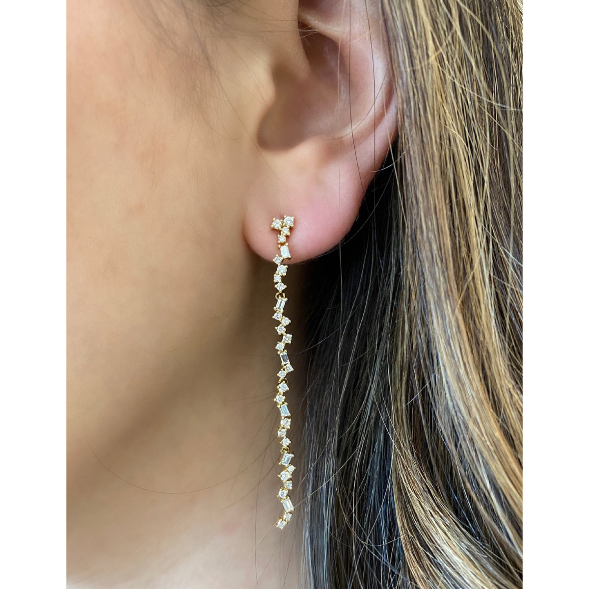 Female Model Wearing Scattered Diamond Dangle Earrings  -14K gold weighing 3.32 grams  -52 round prong-set diamonds totaling 0.75 carats  -12 prong-set straight baguettes totaling 0.31 carats.
