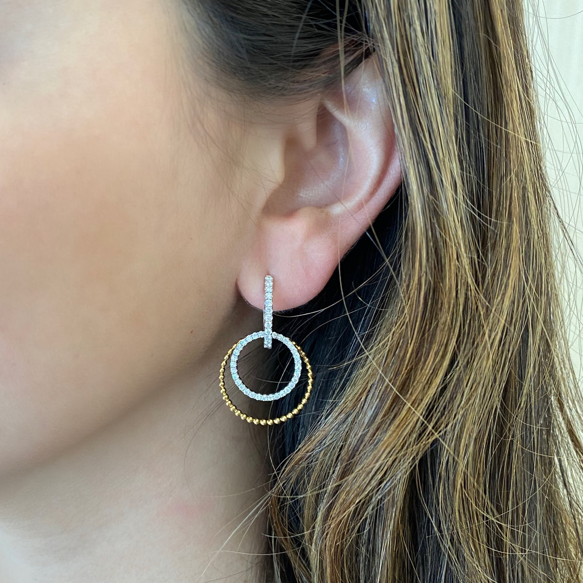 Female model wearing Diamond two-tone double hoop drop earrings -18K gold weighing 6.96 grams -86 round shared prong-set diamonds totaling 0.94 carats.