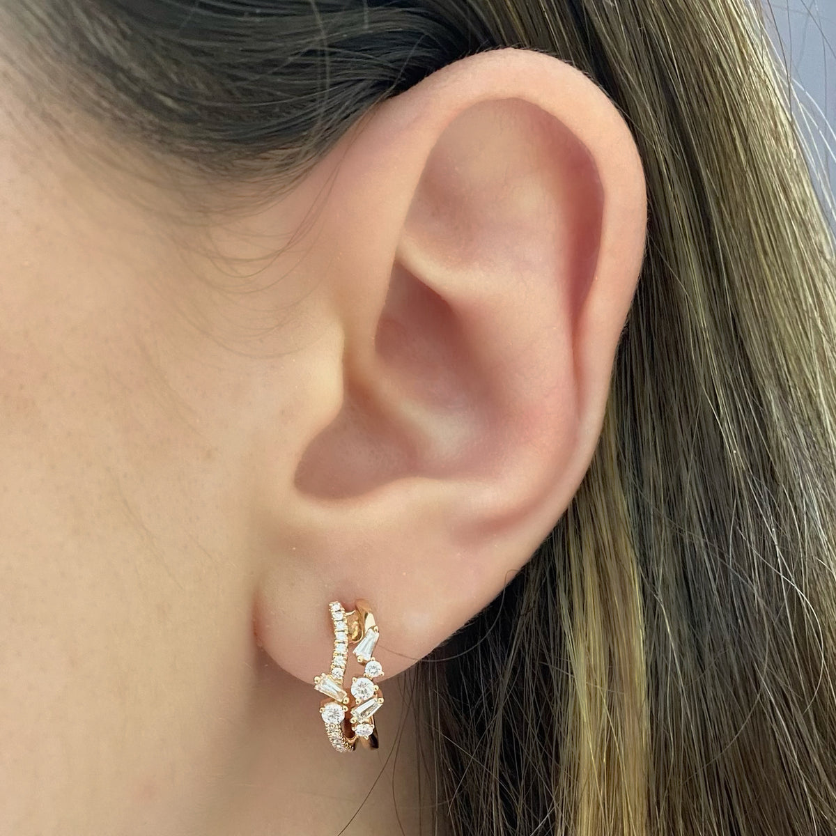 Female model wearing mixed cut diamond huggie earrings - 18K gold weighing 4.43 grams  - 34 round diamonds totaling 0.36 carats  - 6 slim baguettes totaling 0.20 carats