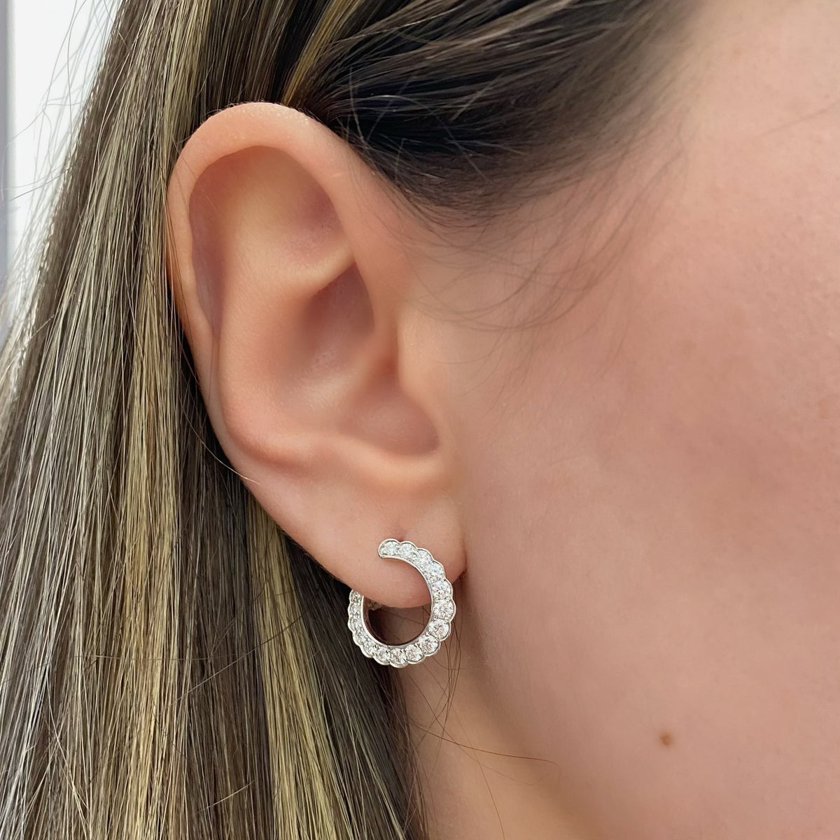 Female model wearing Diamond scalloped front-facing hoop earrings - 18K gold weighing 4.23 grams  - 32 round diamonds totaling 1.02 carats