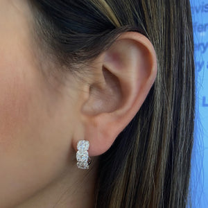 Female Model Wearing Halo Diamond Cushion Huggie Earrings - 18K gold weighing 4.39 grams  - 48 round diamonds totaling 0.99 carats  - 6 round diamonds totaling 0.58 carats