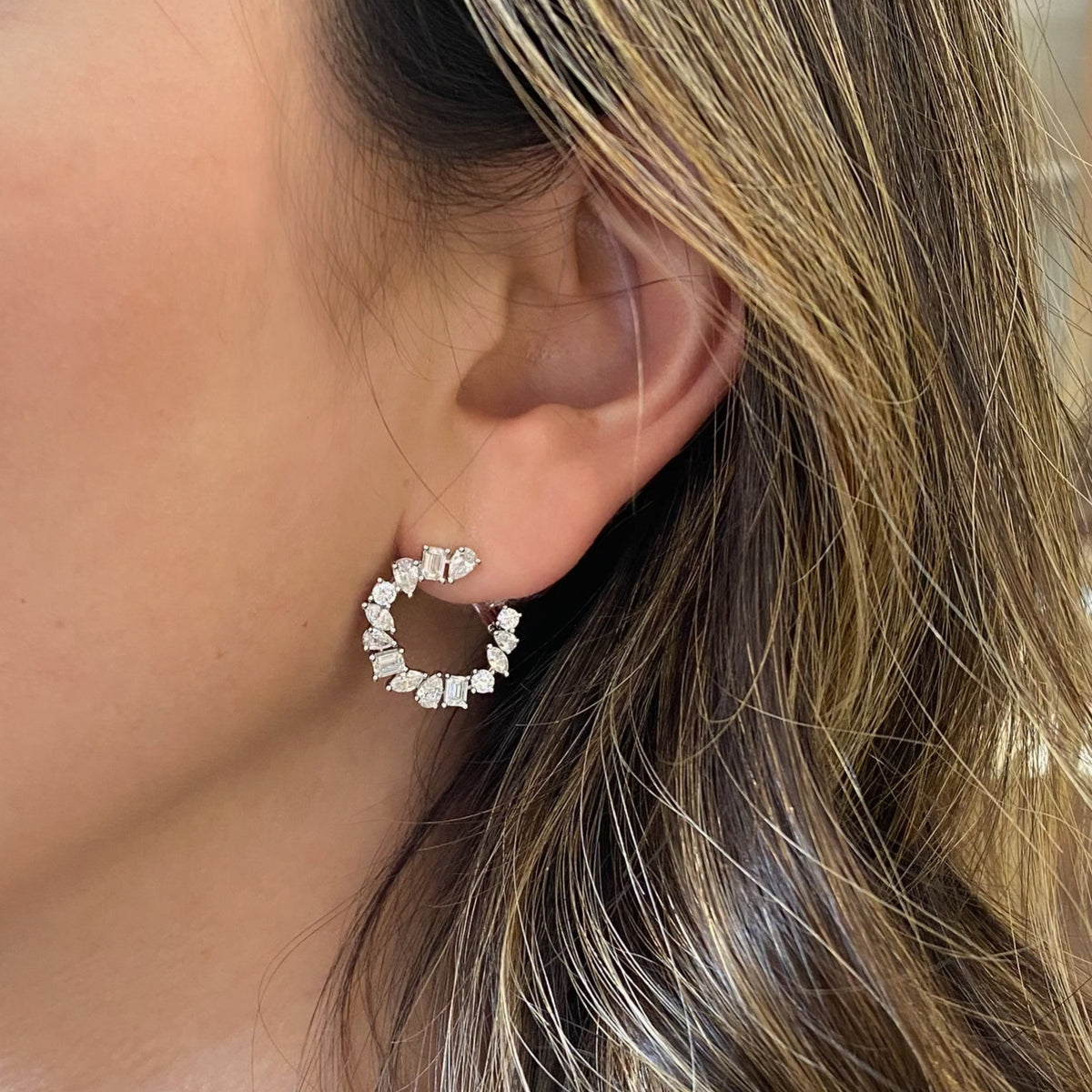 Female model wearing Mixed-Shape Diamond Front-Facing Hoop Earrings - 18K yellow gold weighing 5.5 grams  - 6 marquise-shaped diamonds weighing 0.44 carats  - 6 emerald-cut diamonds weighing 0.87 carats  - 6 round diamonds weighing 0.35 carats  - 12 pear-shaped diamonds weighing 1.05 carats