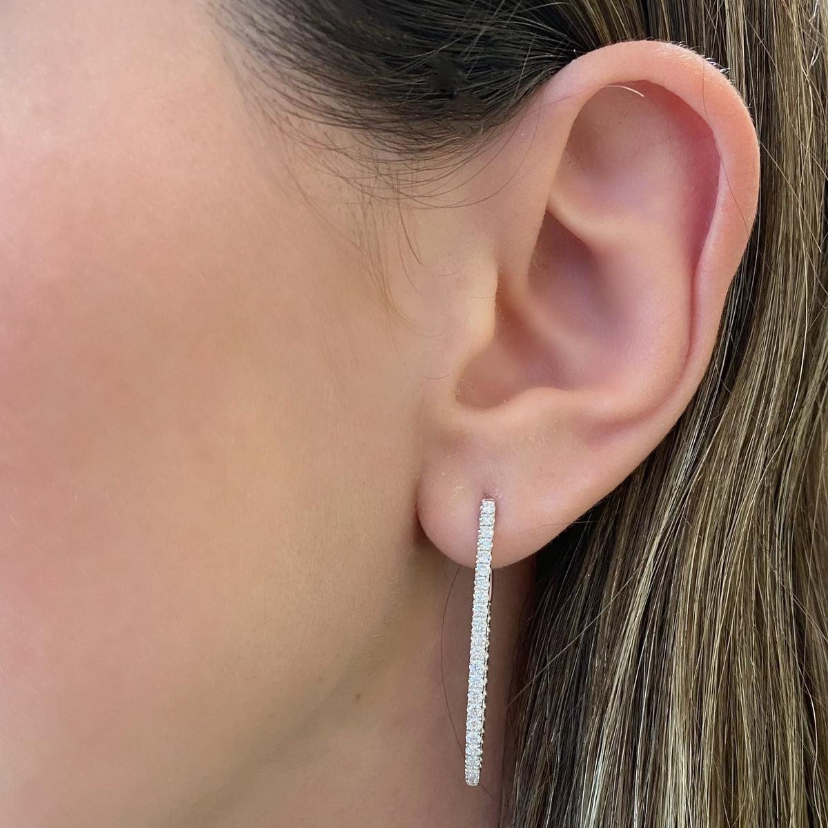 Female model wearing Diamond interior & exterior oval hoop earrings - 18K gold weighing 6.63 grams - 82 round diamonds totaling 1.32 carats