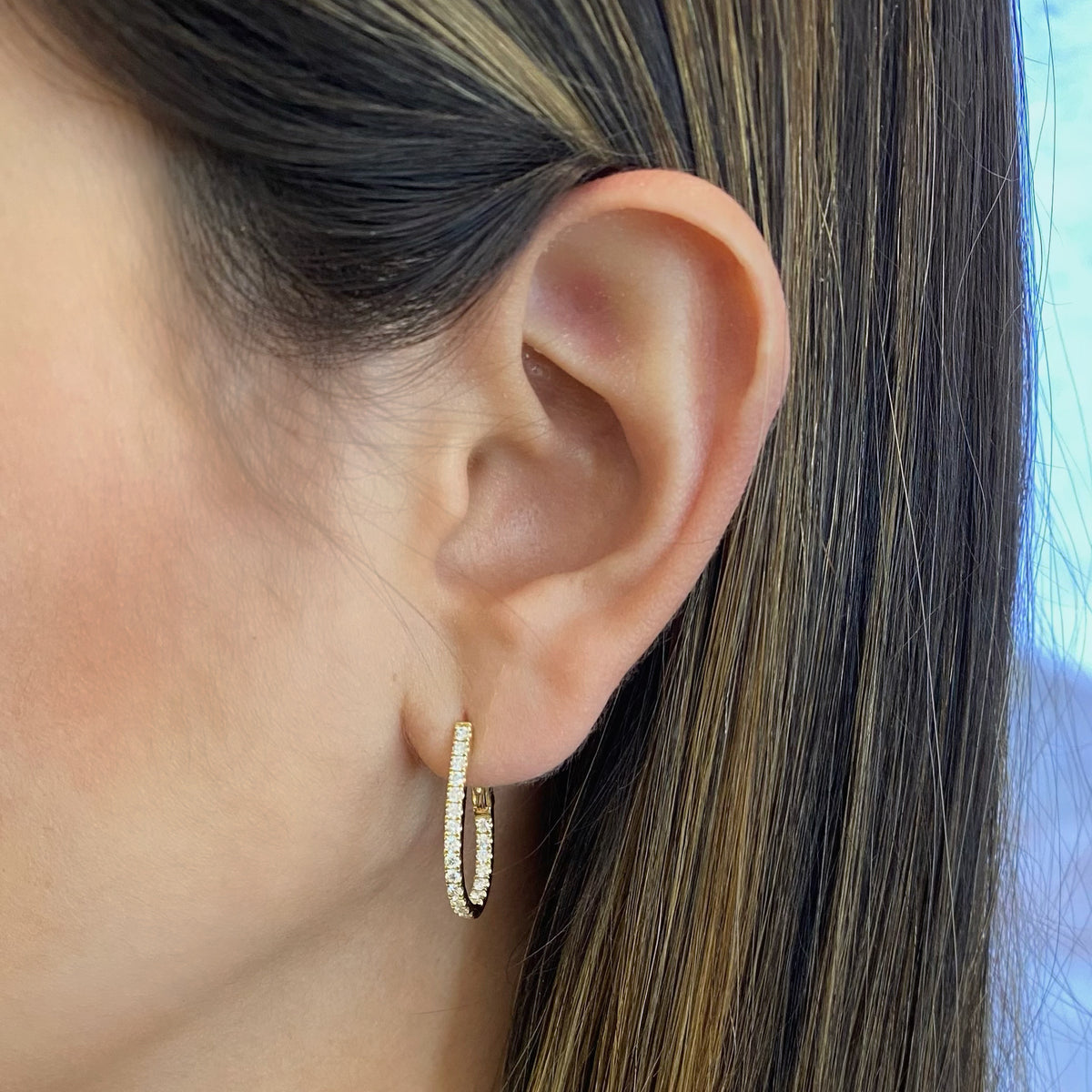 Female model wearing Inside-out diamond oval huggie earrings -18k gold weighing 3.91 grams -44 round diamonds weighing .67 carats