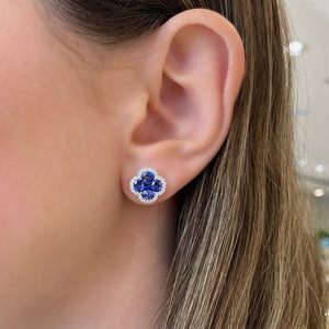 female model wearing sapphire & diamond flower stud earrings - 18K gold weighing 3.37 grams  - 8 oval-shaped sapphires totaling 2.40 carats  - 2 princess-cut sapphires totaling 0.34 carats  - 56 round diamonds totaling 0.28 carats