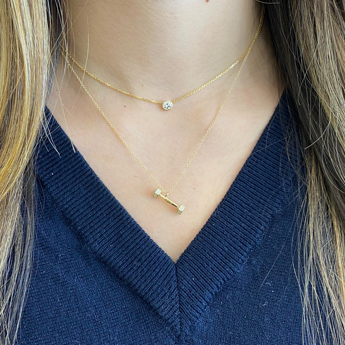 Female model wearing Diamond Dumbbell Pendant - 14K yellow gold weighing 2.54 grams - 72 round diamonds totaling 0.15 carats