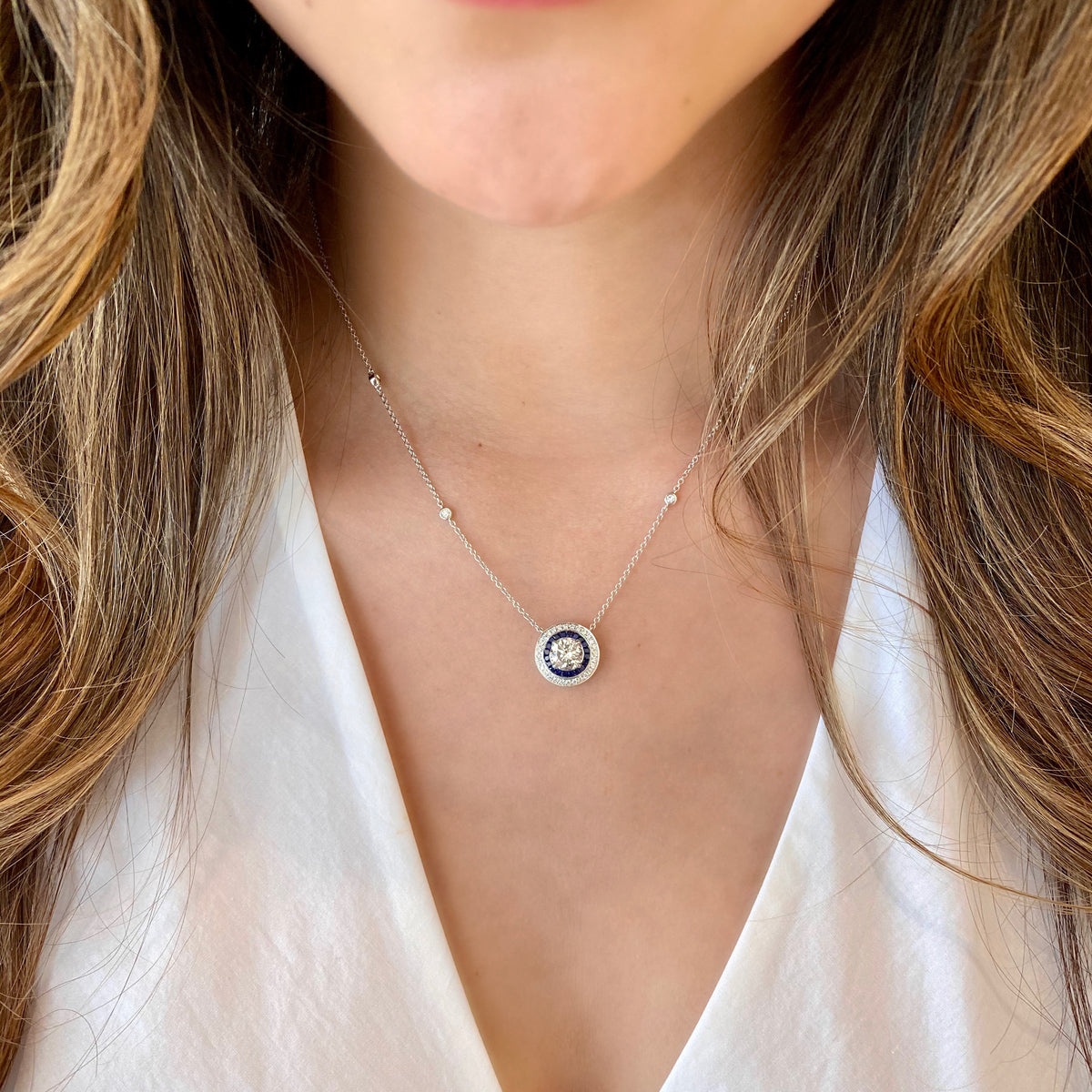 Female Model Wearing Diamond Solitaire Necklace with Sapphires and Bezel-Set Diamond Stations  - 18K gold weighing 5.50 grams  - 1.39 ct round brilliant-cut diamond (GIA-graded G-H color, I2 clarity)  - 20 sapphires totaling 0.59 carats  - 32 round diamonds totaling 0.30 carats