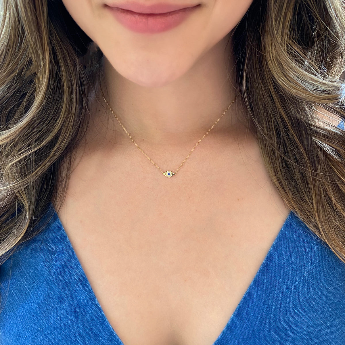 Female model wearing Sapphire & Diamond Evil Eye Pendant  - 14K yellow gold weighing 1.65 grams  - 10 round diamonds totaling 0.02 carats  - 0.03 ct sapphire
