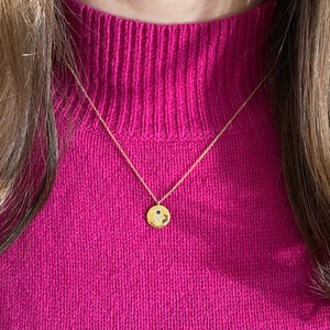 Female model wearing Diamond & Sapphire Hamsa Disc Pendant Necklace -14K gold weighing 3.2 grams -Round pave set diamonds totaling .08 carats -0.04 ct sapphire