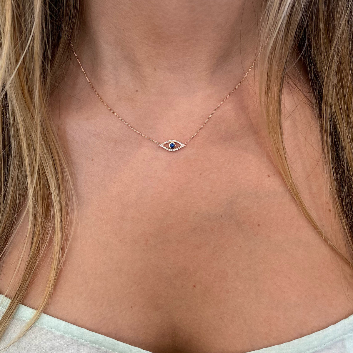 Female model wearing Sapphire & Diamond Open Evil Eye Pendant  - 14K yellow gold weighing 1.77 grams  - 26 round diamonds totaling 0.07 carats  - 0.11 ct sapphire