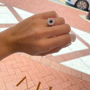 Female model wearing Sapphire double halo ring  - 18K gold weighing 3.88 grams  - 32 round diamonds totaling 0.55 carats  - 21 tapered baguettes totaling 0.51 carats  - 0.82 ct sapphire